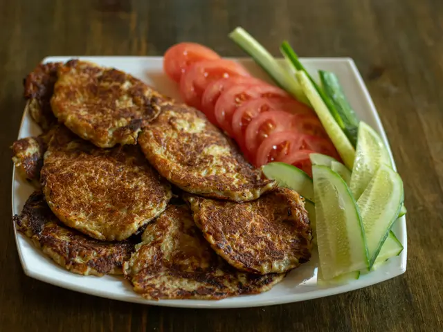 A plate of golden potato pancakes with sliced tomato and cucumber on a wooden table